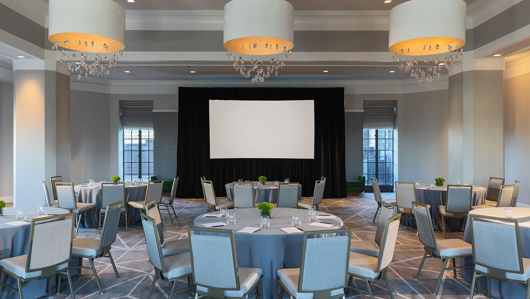 Kimpton Hotel Palomar Philadelphia ballroom with crescent round tables all situated behind a projector screen and underneath 3 identical, circular lighting fixtures