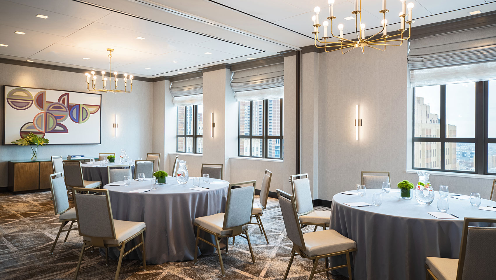 Cret room at Kimpton Hotel Palomar Philadelphia in a rounds meeting set up with multiple round tables that have notepads on top near large sunlit windows overlooking city views