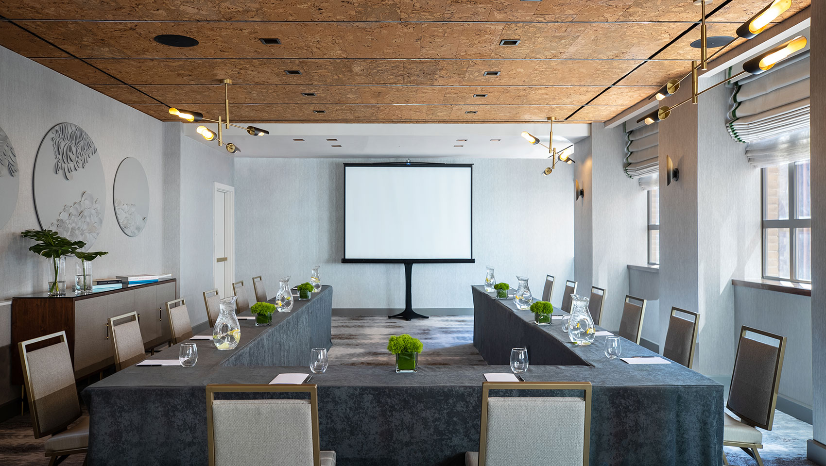 U-shape meeting set up in Tyng room located in Kimpton Hotel Palomar Philadelphia with tables set up in a U-shaped position and a presentation screen towards the back of the room in the center